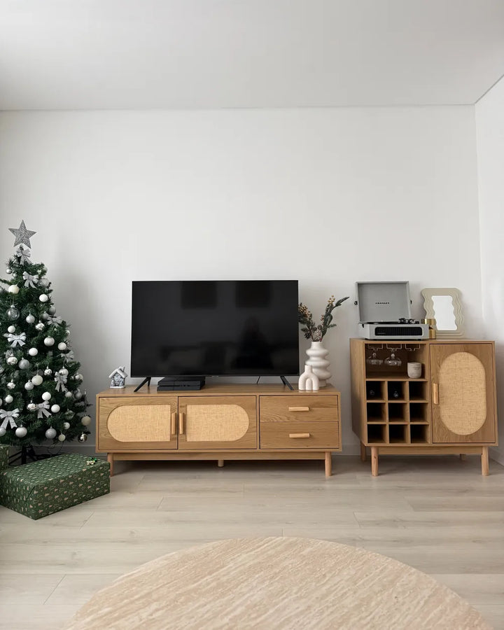 A mid-century modern wooden TV stand and matching cabinet with woven cane panels, styled in a minimalist living room next to a Christmas tree and a black television.