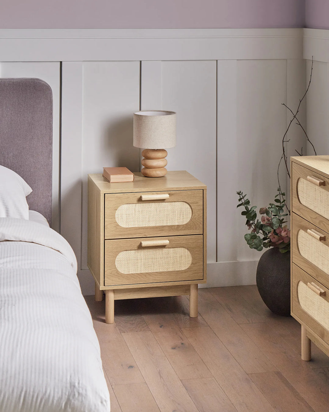 Wooden nightstand with lamp and books next to a bed in a bedroom.