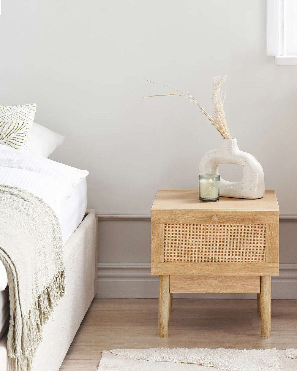 Wooden bedside table with decorative items next to a bed in a bedroom.