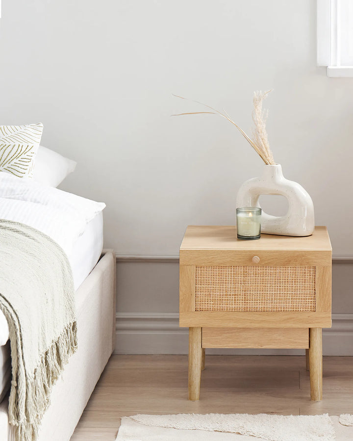 Wooden bedside table with decorative items next to a bed in a bedroom.