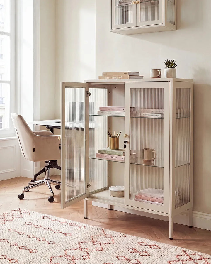 A tall cream-colored storage cabinet with two glass doors and ribbed glass panels, styled in a bright home office next to a desk and chair.