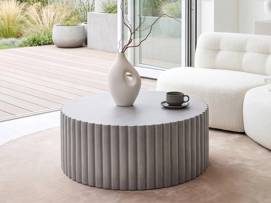 Round pleated coffee table with a white vase and black mug in a modern living room.