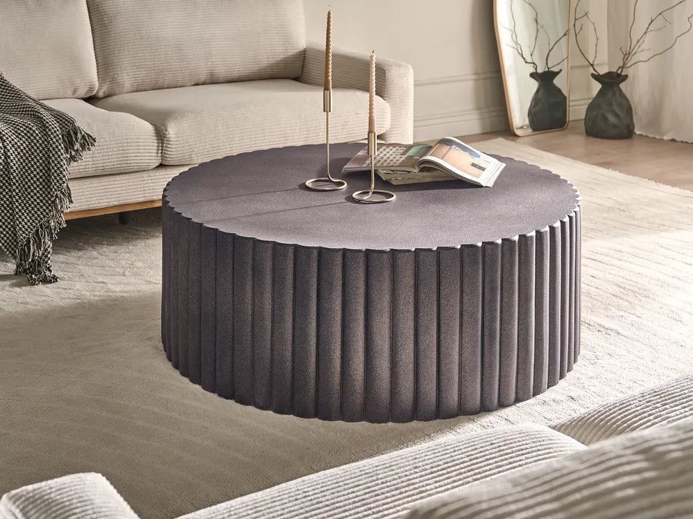 Round textured coffee table in a living room setting with a couch and decorative items.