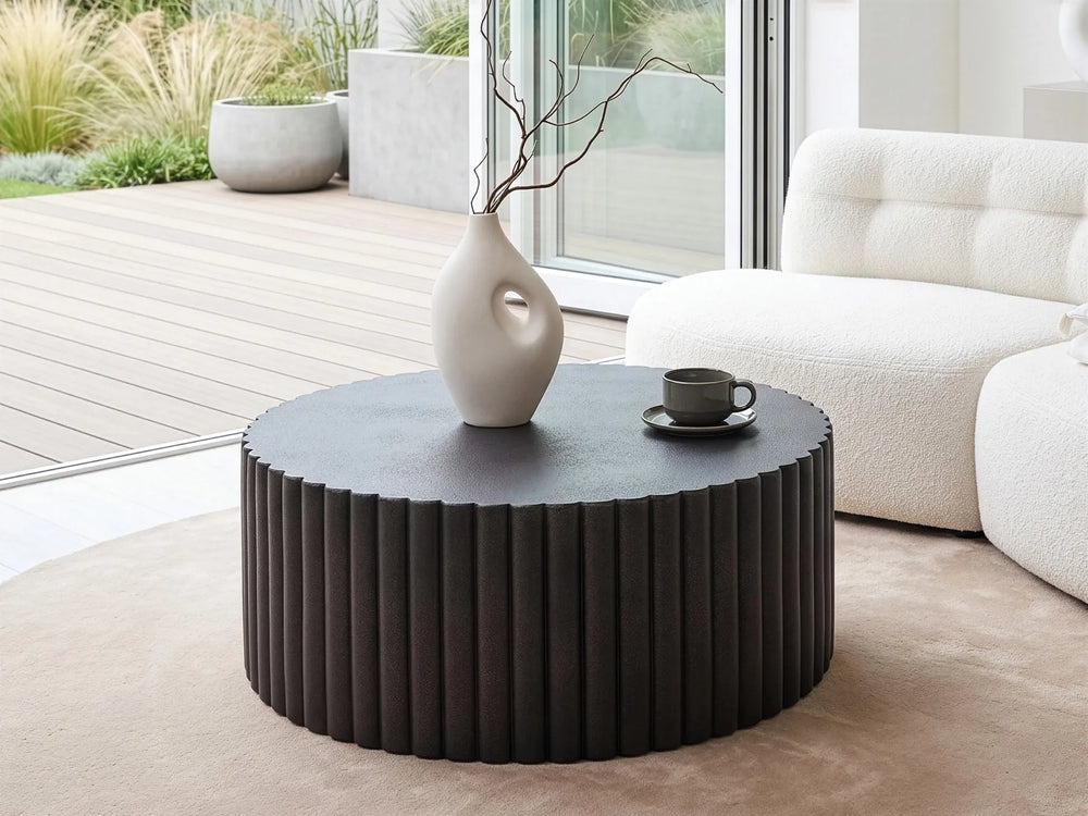 Round black coffee table with a white vase and small black cup in a modern living room.