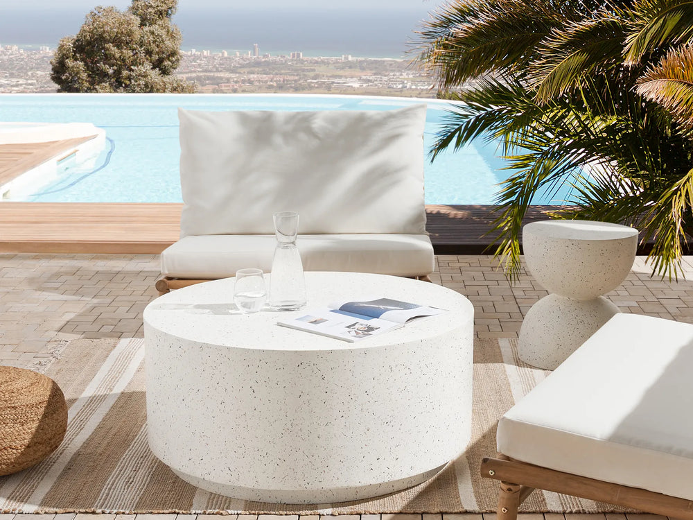 Outdoor patio setting with white furniture and a pool in the background