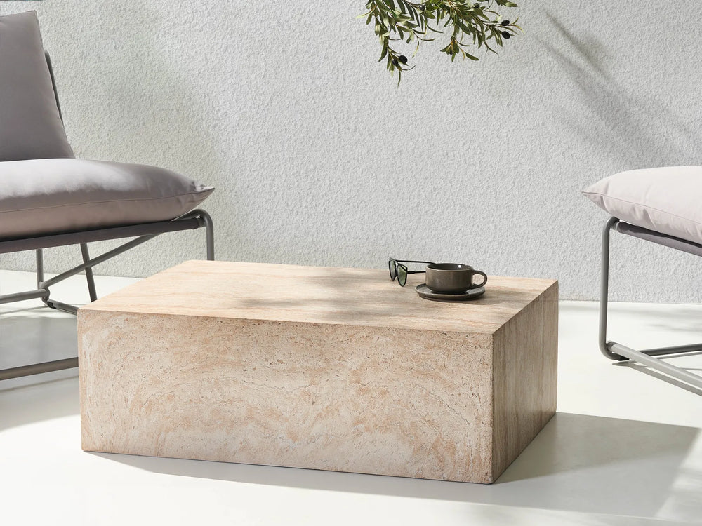 Beige marble coffee table in a modern living room setting with a chair and plant.