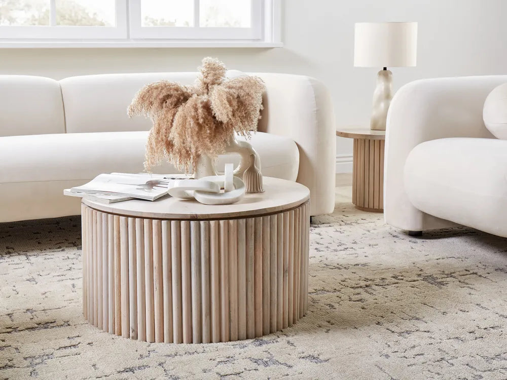 Round wooden coffee table in a living room with a white sofa and decorative items.