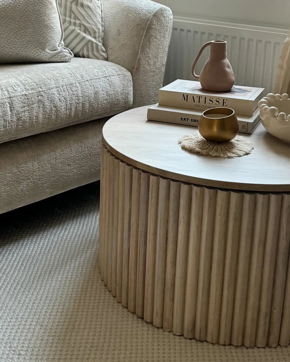 Round wooden coffee table with decorative items in a living room setting.