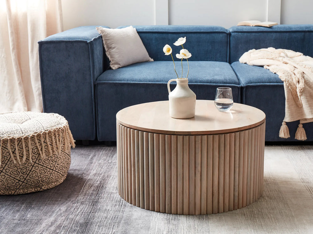 Modern living room with a blue sectional sofa, round wooden coffee table, and decorative items.