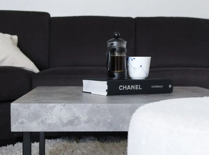 Black sofa with a coffee table featuring a Chanel book, a French press, and a white mug.