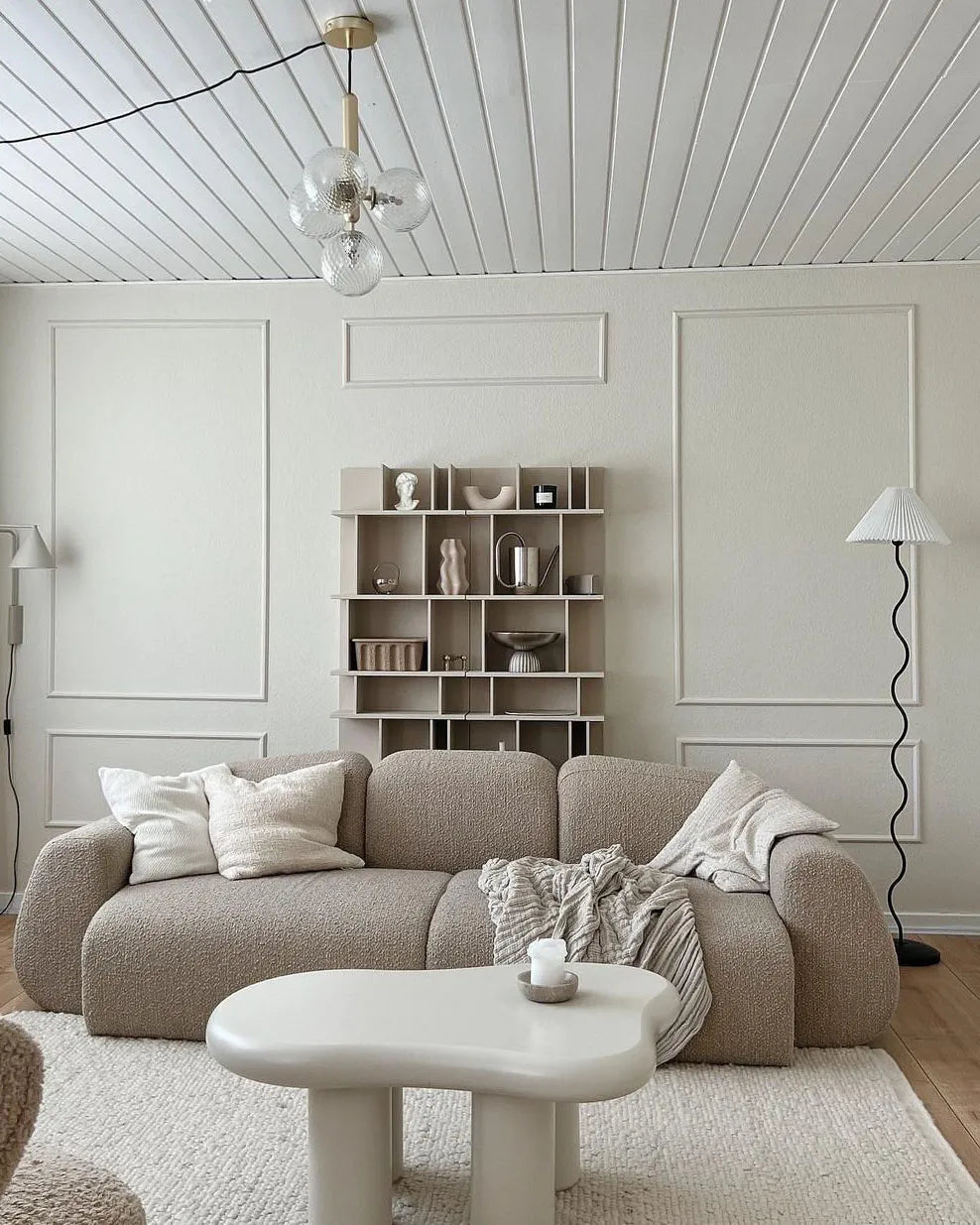 Modern living room with a beige sofa, white coffee table, and bookshelf.