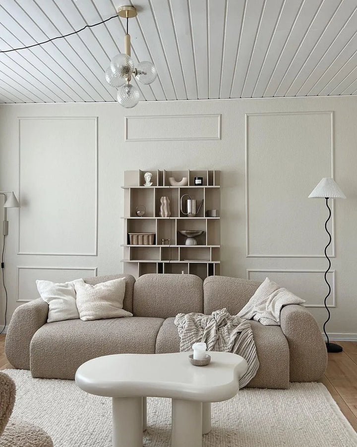 Modern living room with a beige sofa, white coffee table, and bookshelf.