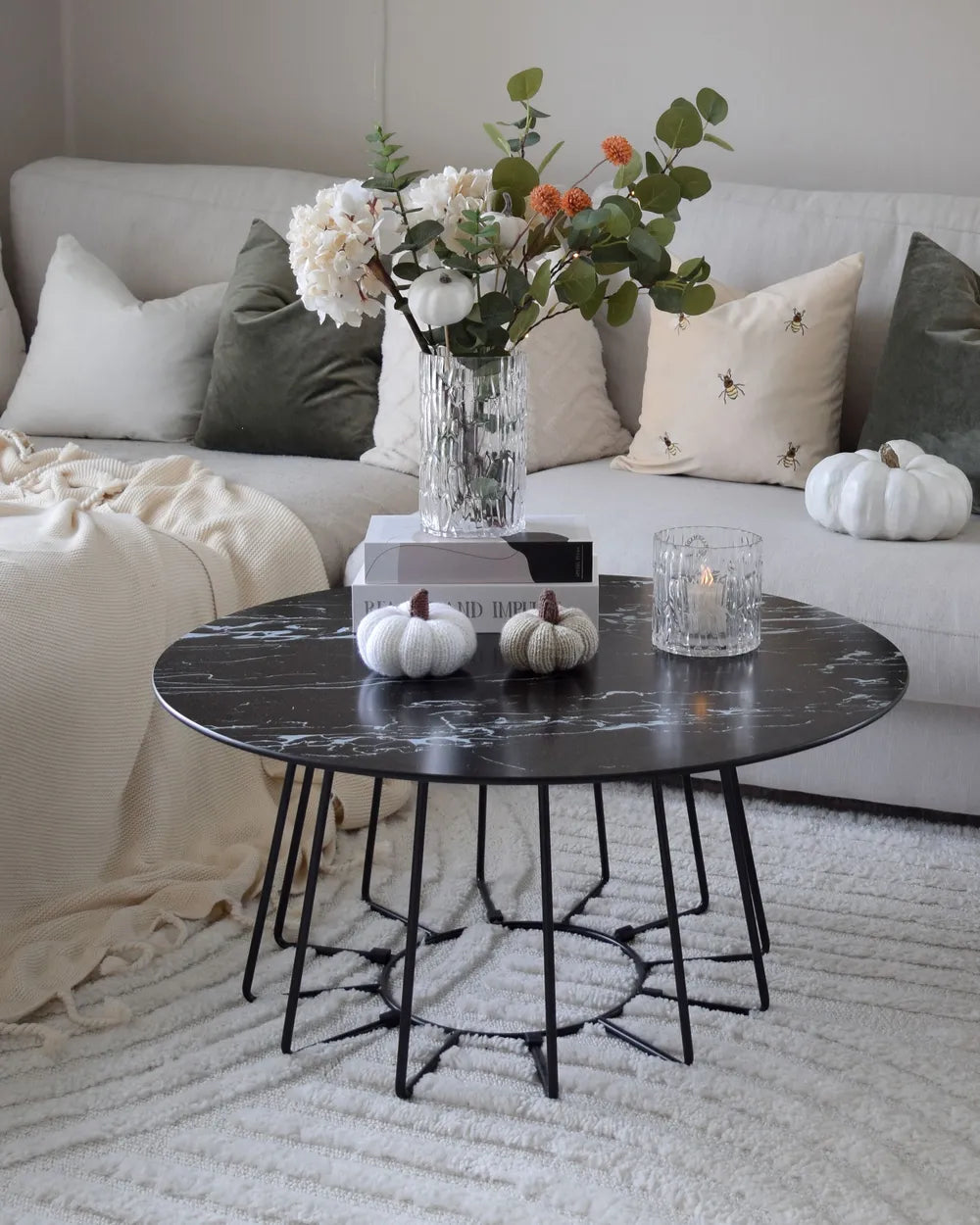 Living room with a black marble coffee table, white pumpkins, and a vase of flowers.