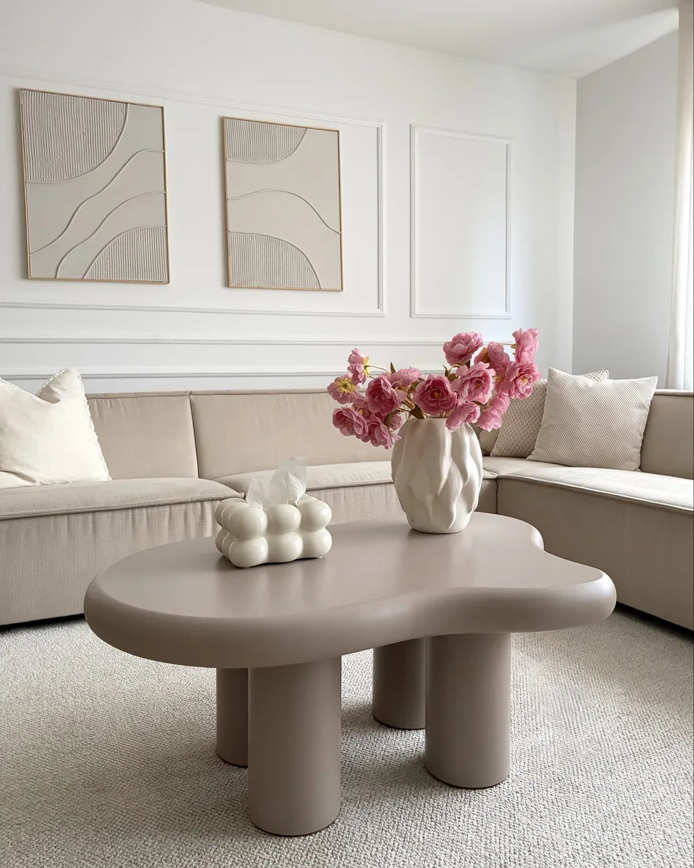 Modern living room with a beige sectional sofa, coffee table, and decorative elements.