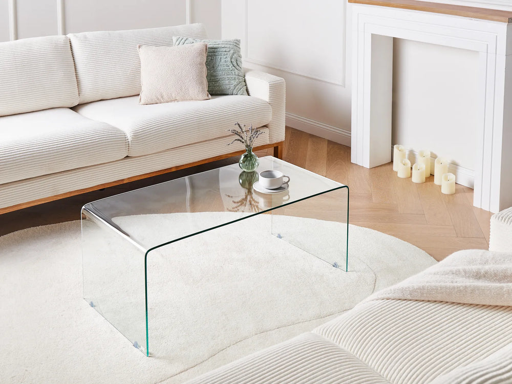 Modern living room with a glass coffee table, white sofa, and decorative candles.