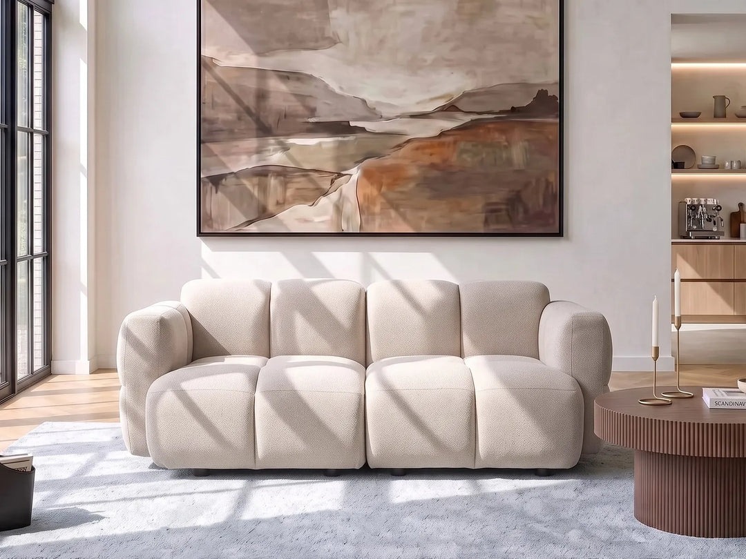 A modern cream-colored modular sofa with a unique segmented, bumpy texture, styled in a bright, contemporary living room under a large abstract landscape painting.