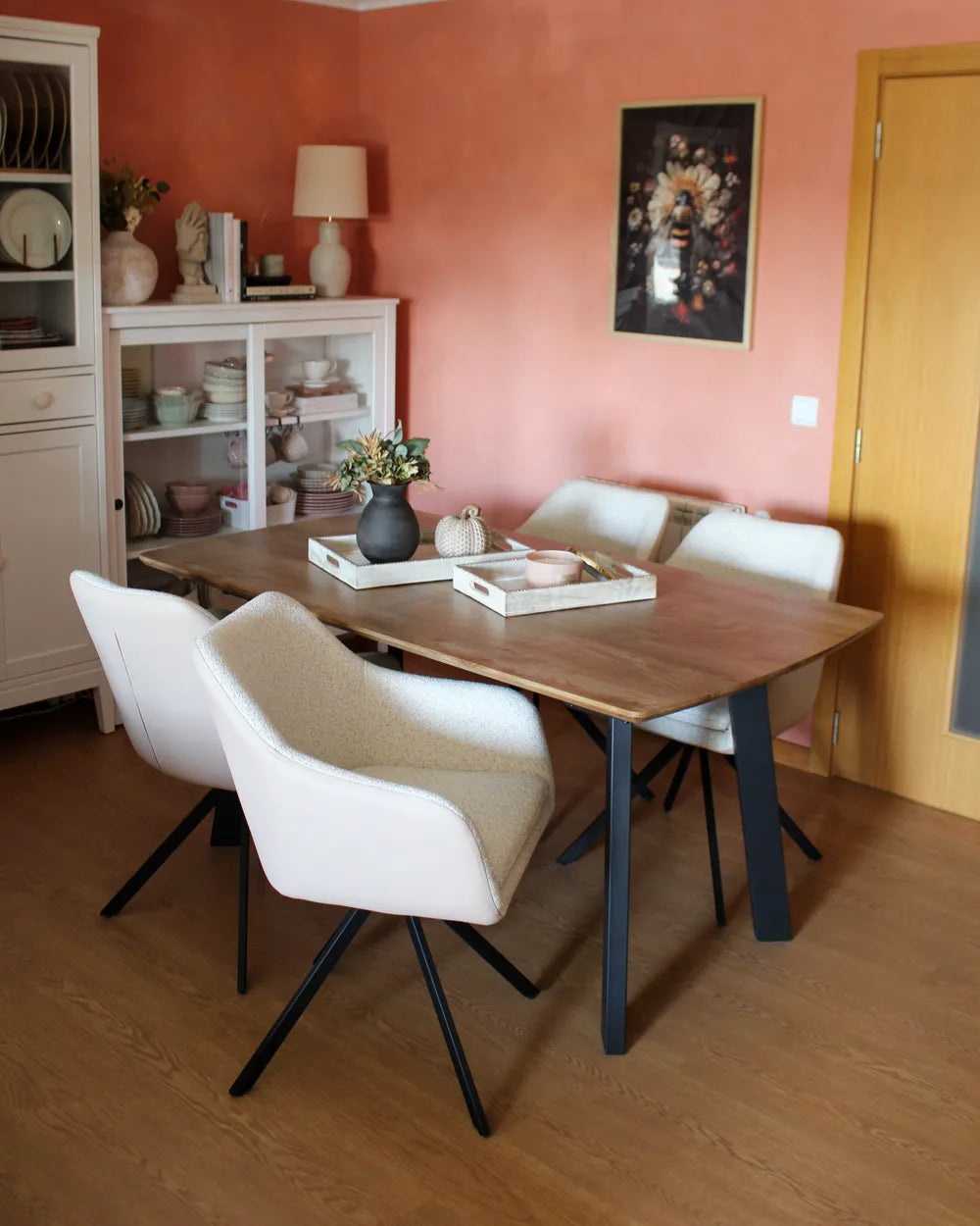 Dining room with a wooden table and white chairs against a pink wall.