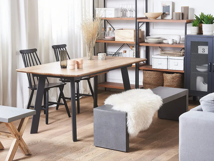 Dining area with wooden table, chairs, and a gray ottoman in a home setting.