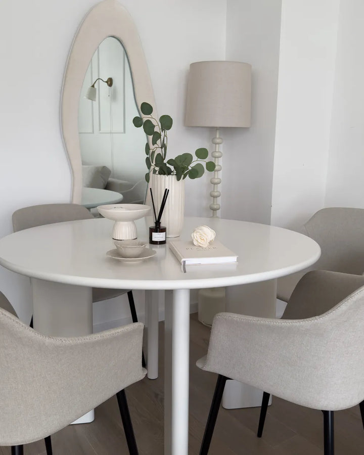 Dining room with a round white table and gray chairs, featuring a lamp and decorative items.