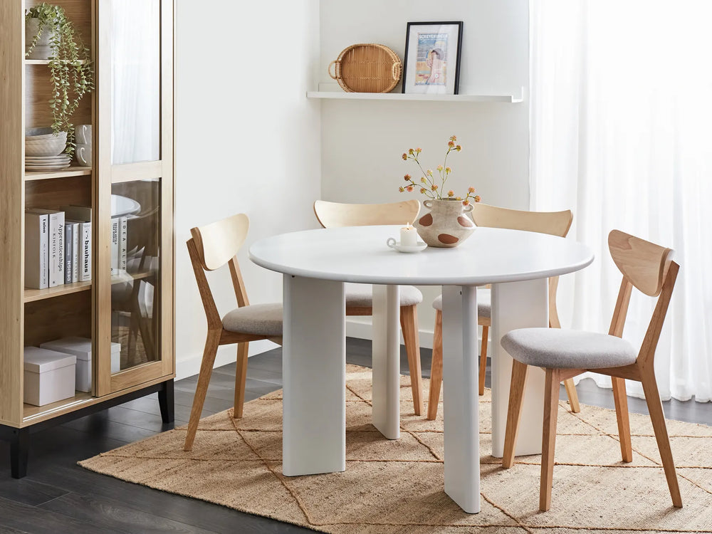Dining room with a white round table and wooden chairs on a beige rug.