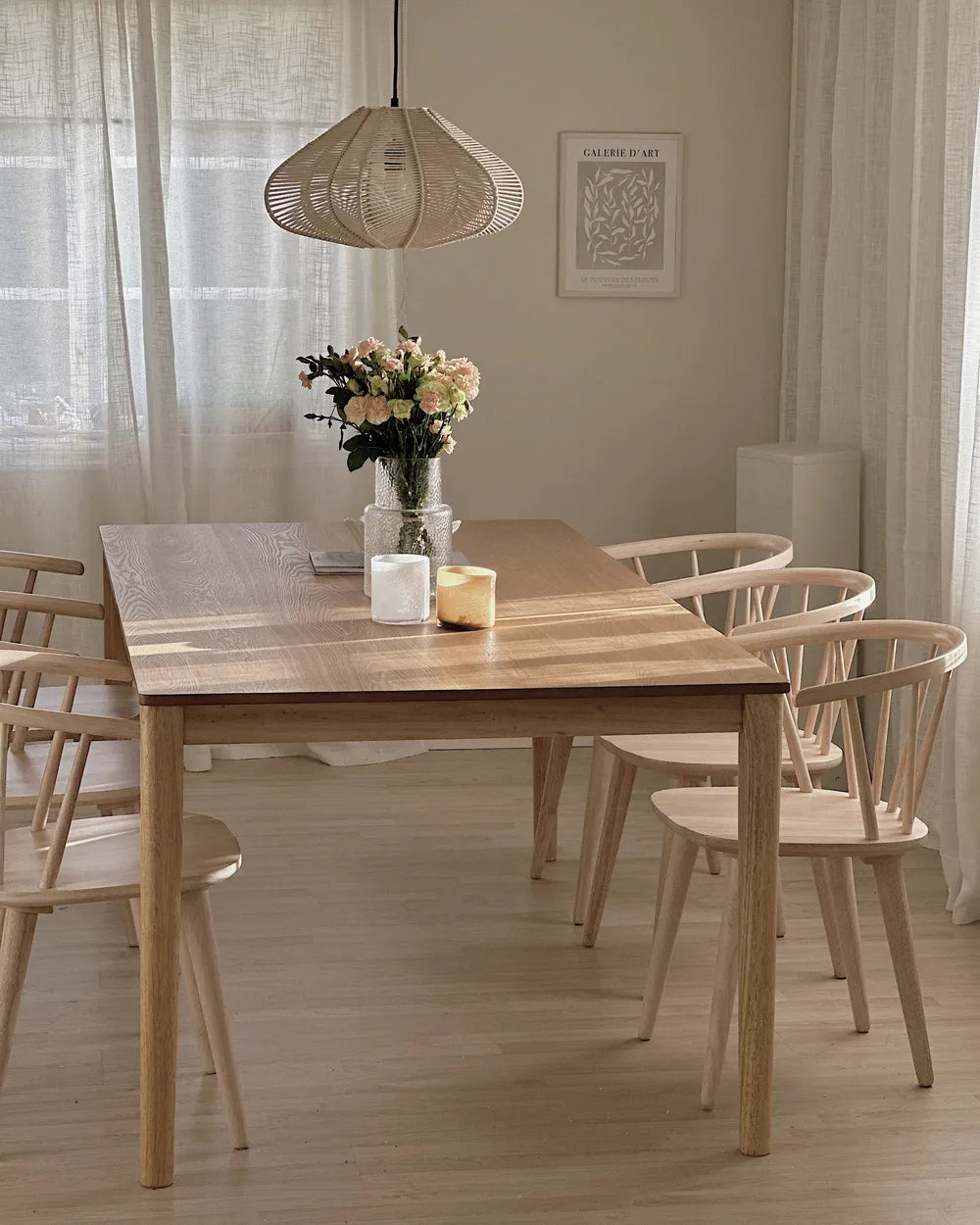 Dining room with wooden table and chairs, featuring a vase of flowers and a candle.