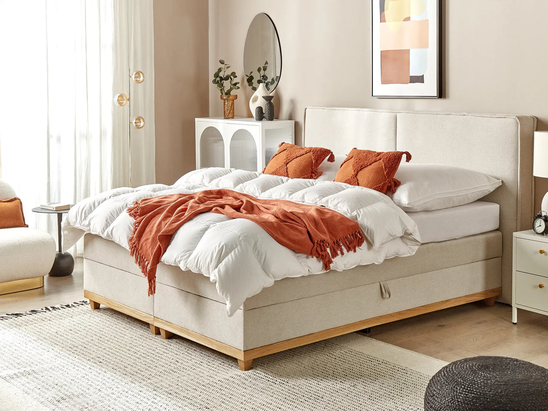 Beige bed with white bedding and orange throw in a bedroom setting.