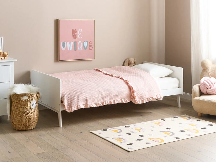 Children's bedroom with a white bed, pink bedding, and 'Be Unique' poster.
