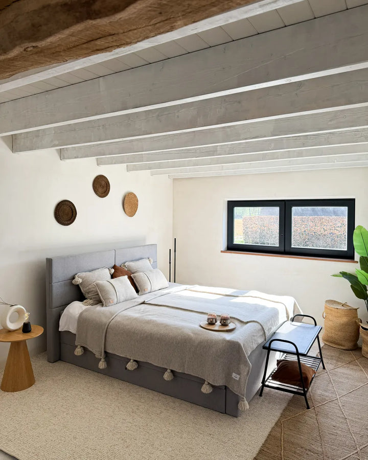 Modern bedroom with gray bed, wooden side table, and decorative elements.