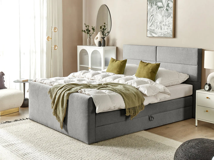 Gray upholstered bed with white bedding and green pillows in a bedroom setting.