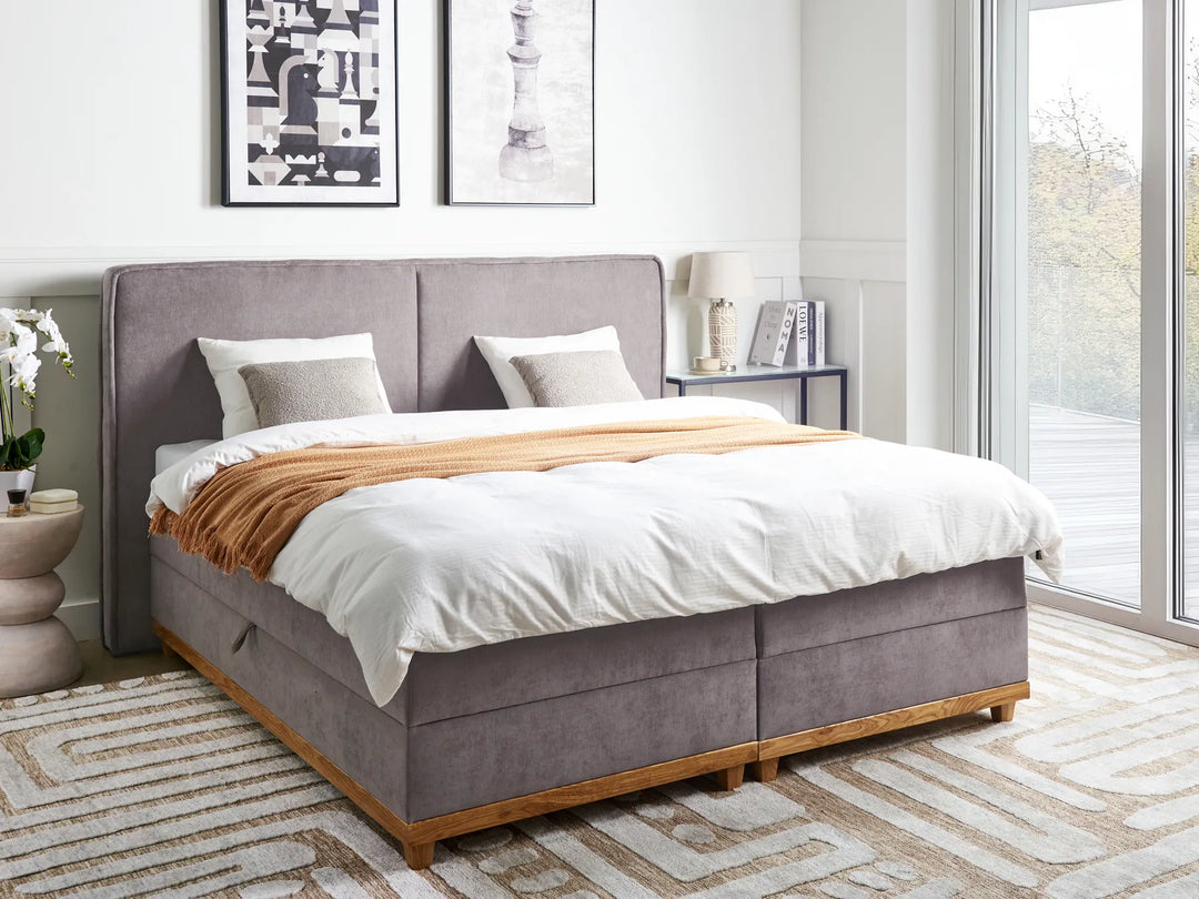 Gray upholstered bed with white bedding and a wooden base in a modern bedroom.