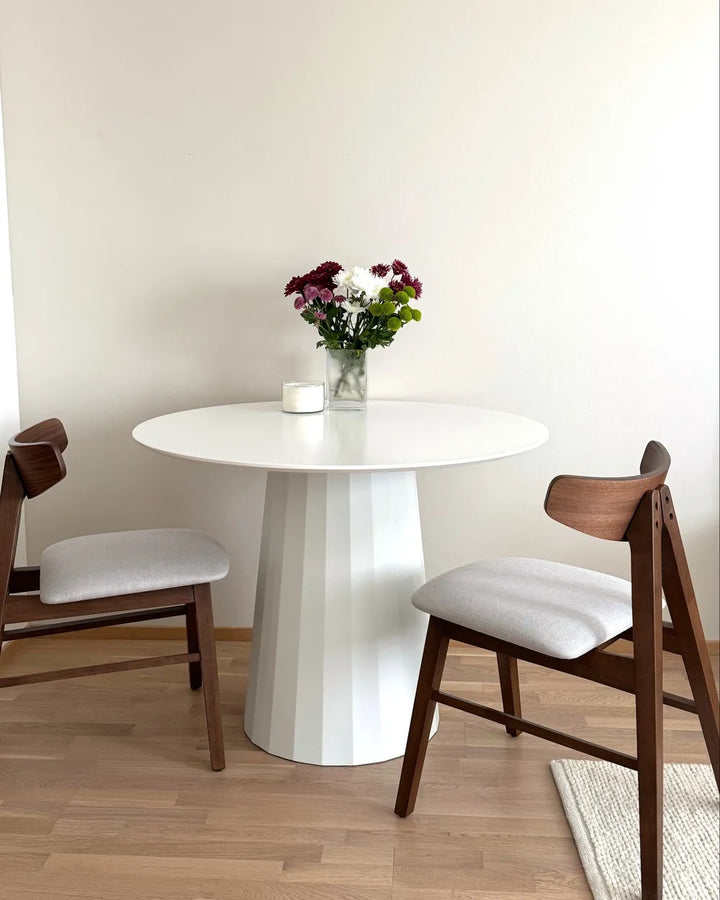 Round white dining table with wooden chairs and a vase of flowers on a light wood floor.