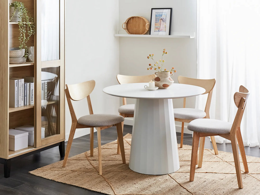 Dining room with a round white table and wooden chairs on a beige rug.