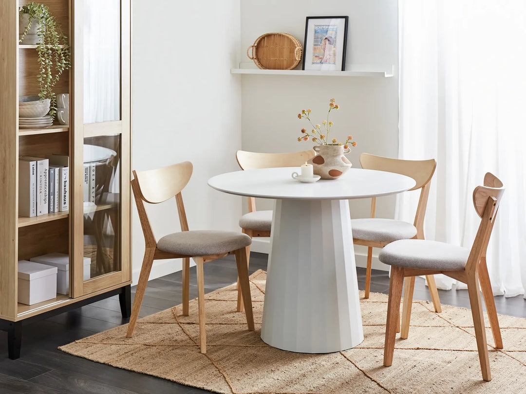 Dining room with a round white table and wooden chairs on a beige rug.