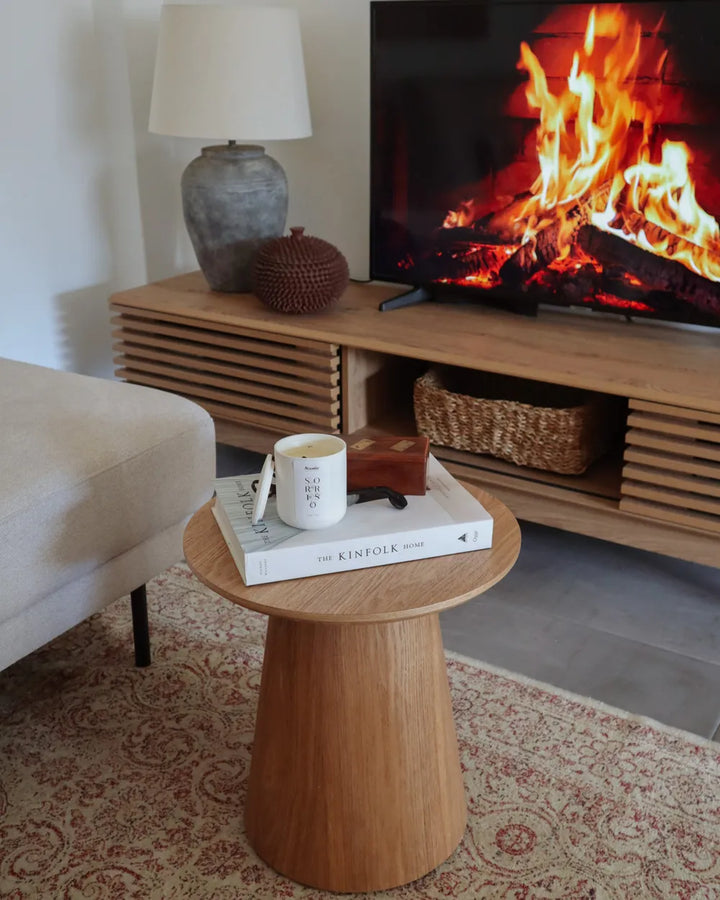 Living room with a wooden side table, lamp, and TV displaying a fire.