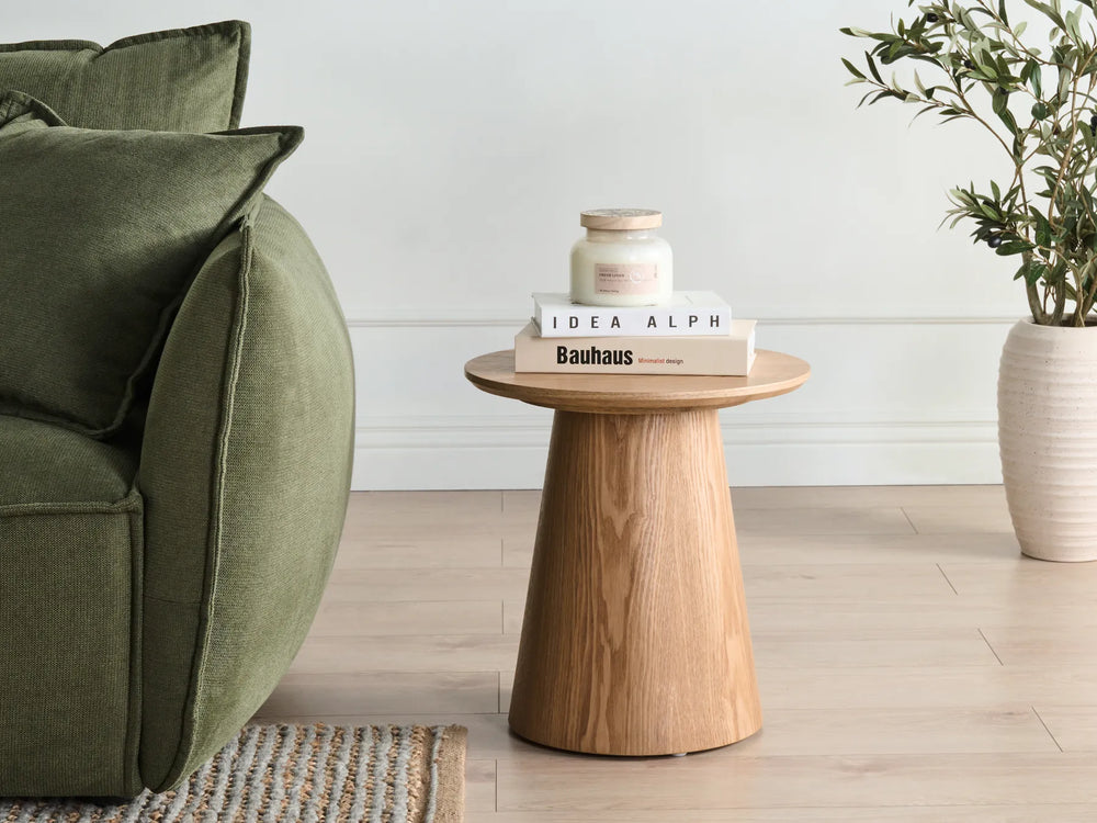 Wooden side table with books and a candle next to a green sofa in a living room.