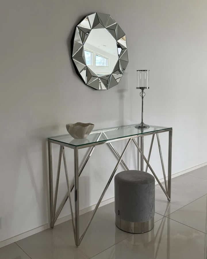 Modern glass console table with metal frame, decorative mirror, and candle holder against a plain wall.