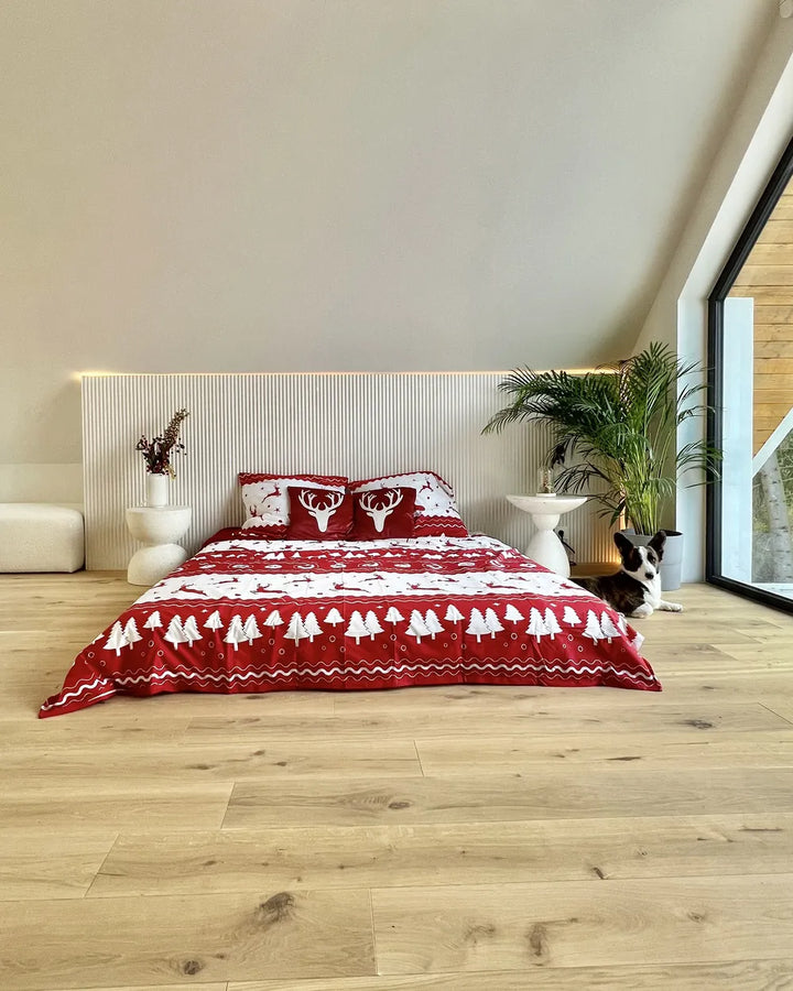Bedroom with a red and white patterned bedspread on a bed, wooden floor, and plants.