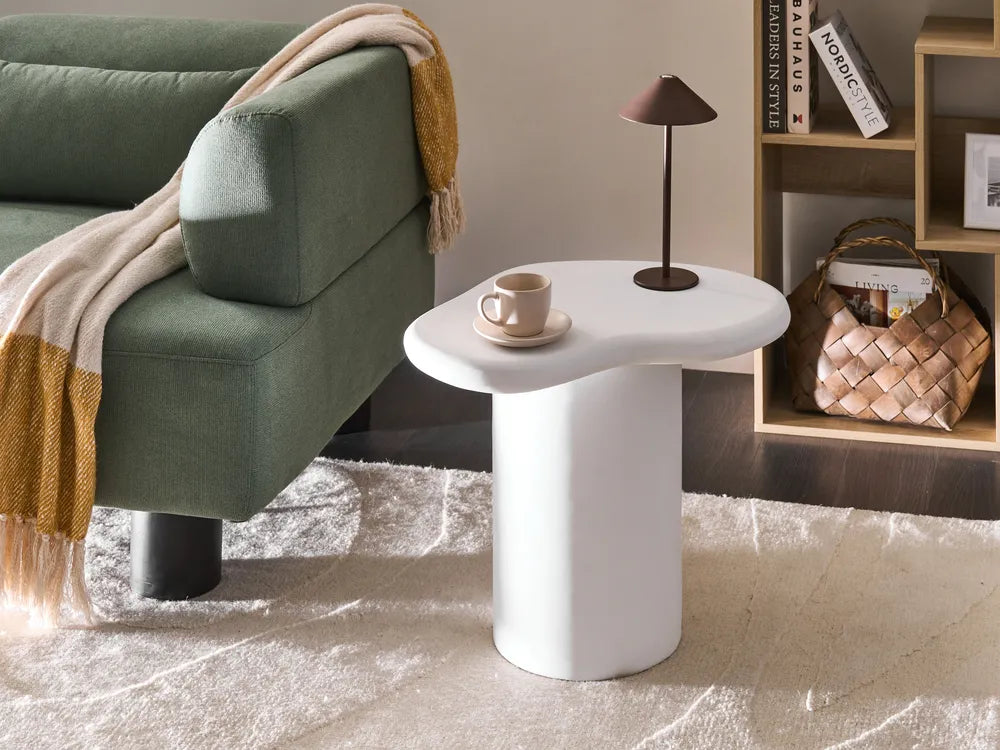 Green sofa with a blanket, white side table with a cup and saucer, and a lamp in a room setting.