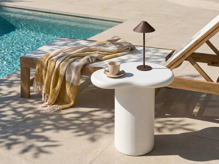 White side table with a cup and saucer next to a poolside lounge chair with a yellow blanket.