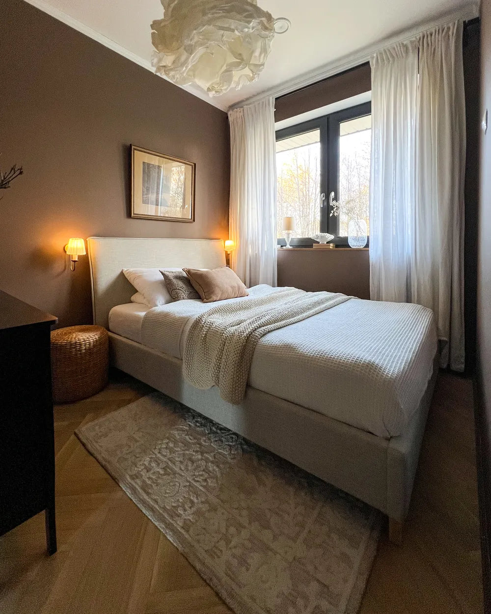 Neatly made bed in a bedroom with a lamp, rug, and window.