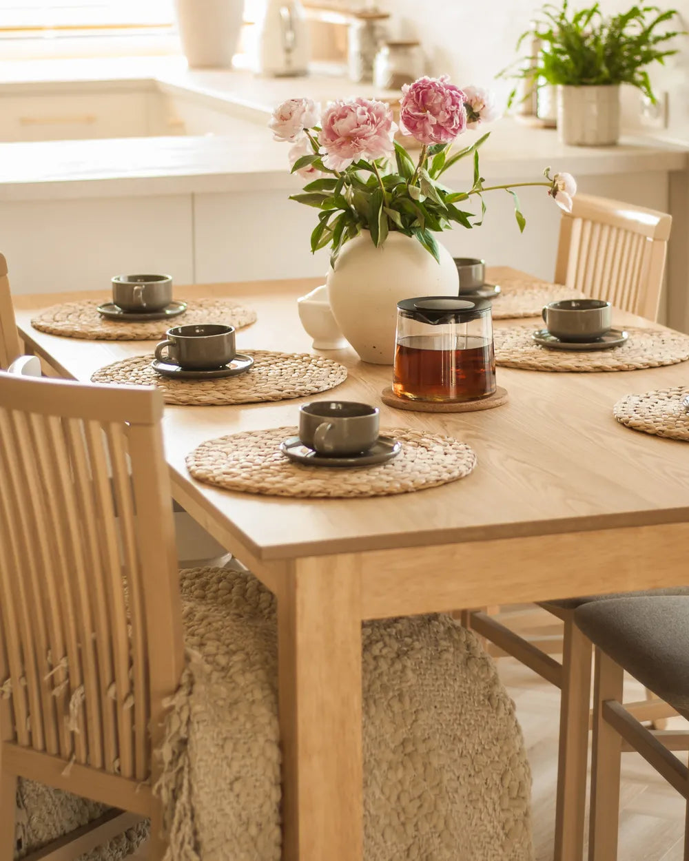 Dining table set with teacups, a vase of flowers, and placemats in a kitchen.