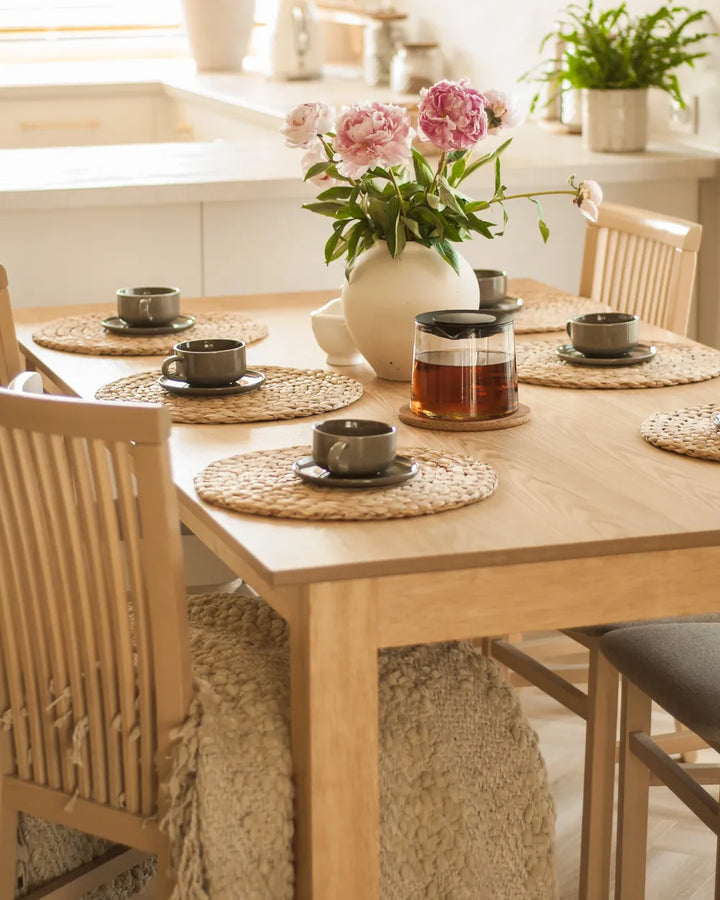 Dining table set with teacups, a vase of flowers, and placemats in a kitchen.