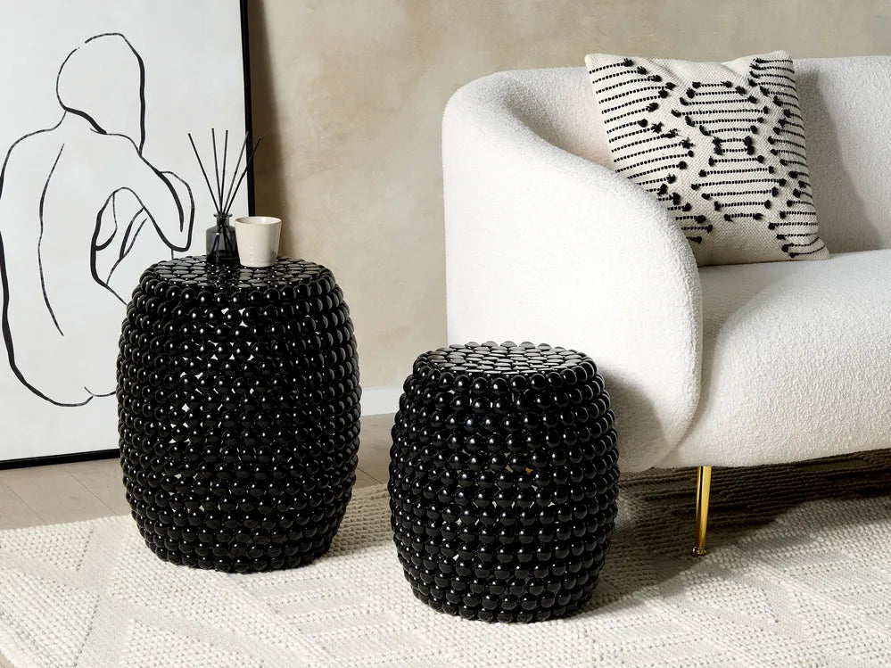 Two black beaded stools in front of a white sofa with a decorative pillow.
