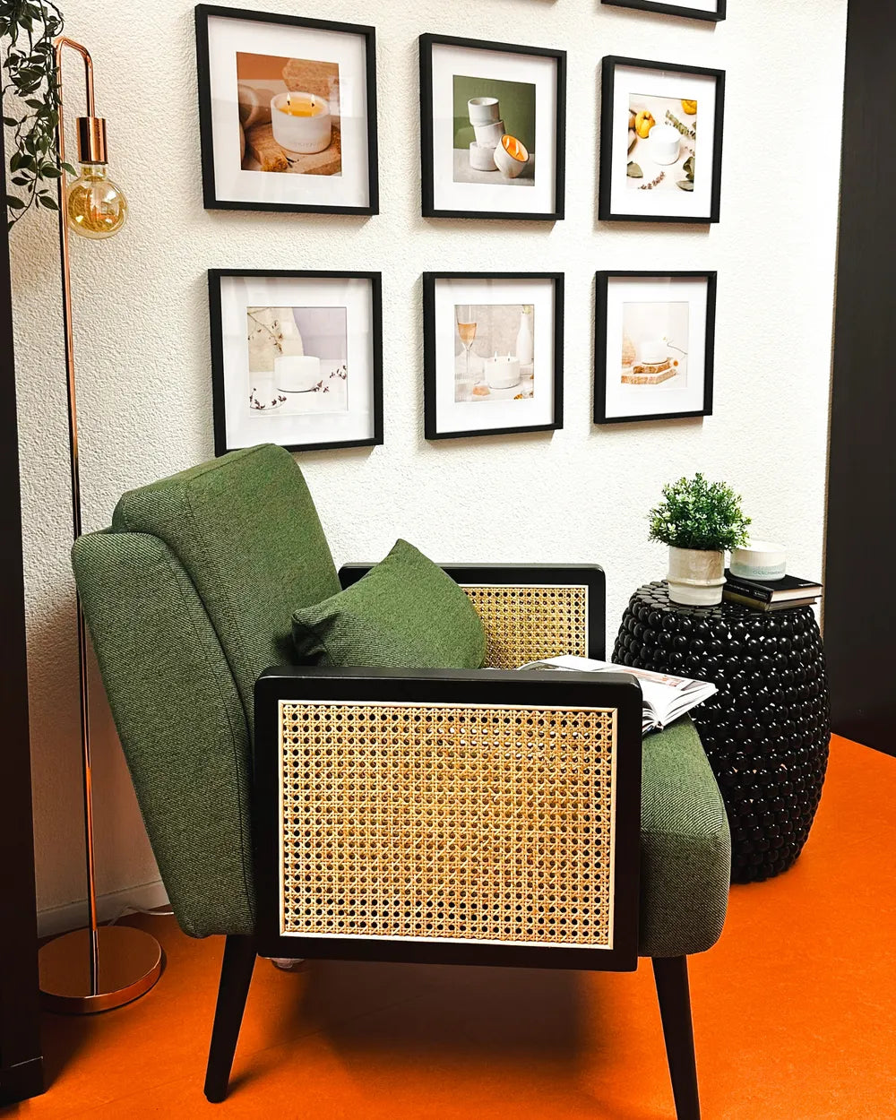 Green armchair with wicker backrest in a room with orange floor and framed pictures on the wall.