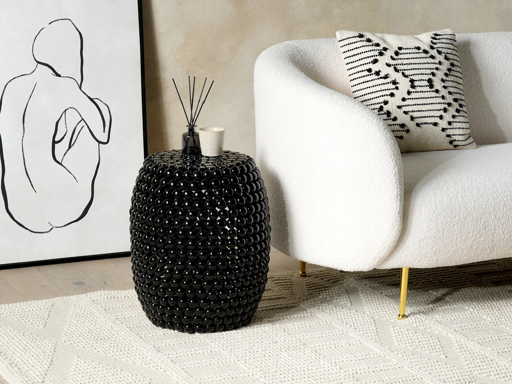 Black beaded side table next to a white sofa with a decorative pillow in a living room setting.