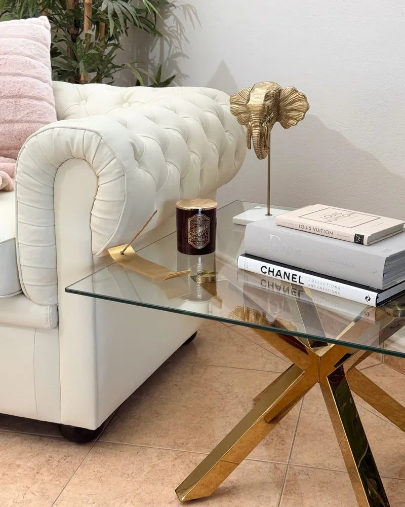 Glass coffee table with gold legs next to a white sofa in a living room setting.