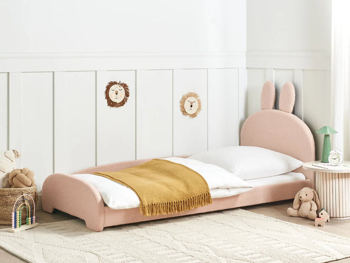 Children's pink bed with bunny ears in a room with white walls and toys.