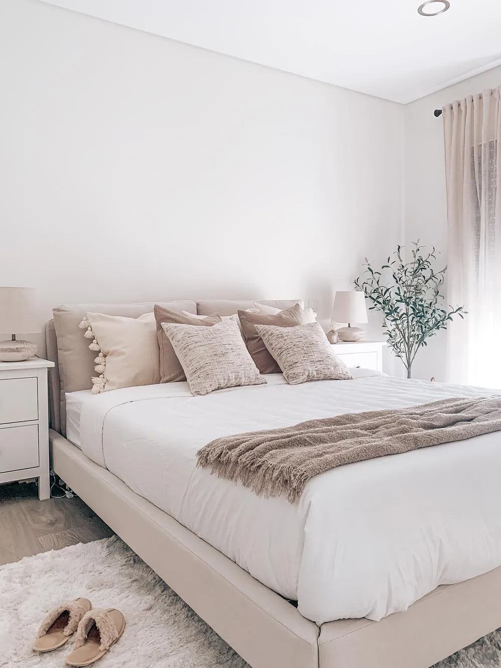 Neatly made bed with beige pillows and a blanket in a bedroom setting.