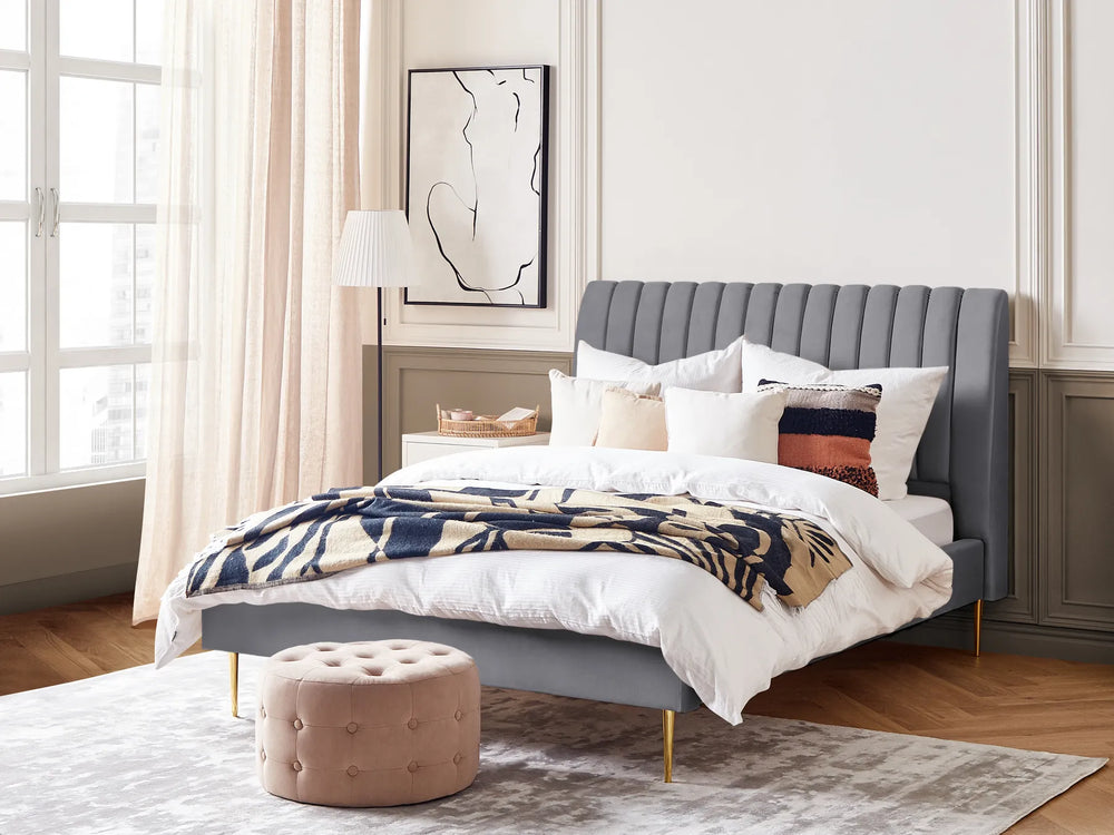 Modern bedroom with a gray upholstered bed, white bedding, and a beige ottoman.