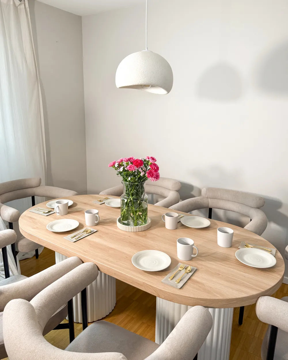 Dining room with a round wooden table set for a meal, featuring plates, cups, and a vase with flowers.